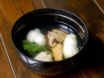 椀物（松茸と鱧のお吸い物）[b]今日の椀物は、季節の変わり目らしく秋の走りと夏の名残です。秋の松茸と夏の鱧の湯引きを上品に味付けしたお吸い物でどうぞ。エビと菊科の新芽が彩りを加えています。